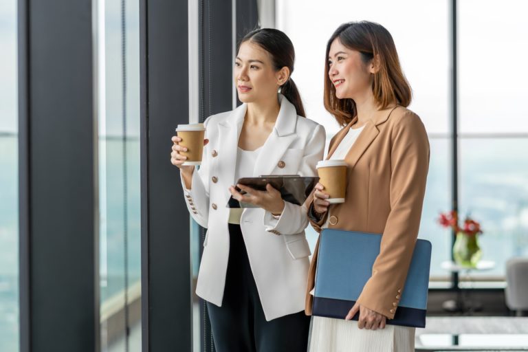 Two asian businesswomen talking during coffee break in modern office or coworking space