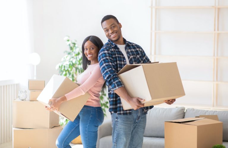 Young black homeowners with carton boxes feeling happy in their new home on moving day, panorama