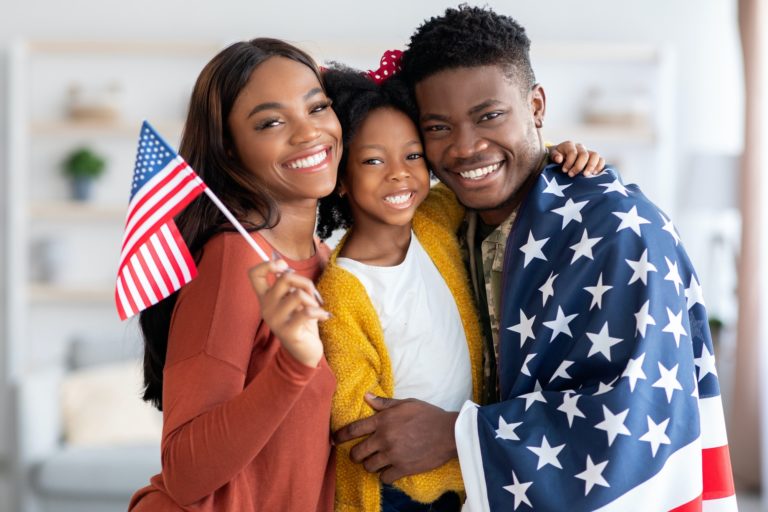 Black military man wrapped in flag posing with wife and little daughter